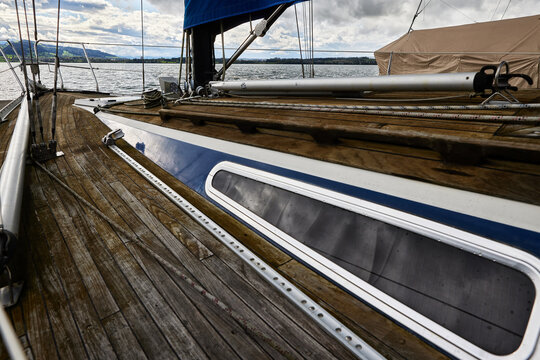 Sailing yacht teak deck with rigging, boom, and side window facing lake view. Wooden sailboat deck detail, nautical equipment, marine transport, and luxury vessel lifestyle