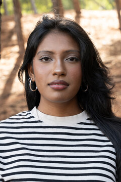Confident young woman in striped shirt standing outdoors in natural sunlight
