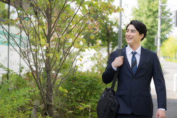 屋外の道路を歩きながら営業の外回りや取引先への訪問に向かうスーツ姿の日本人男性サラリーマン、法人営業のイメージ上半身 © kapinon