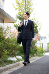 屋外の道路を歩きながら営業の外回りや取引先への訪問に向かうスーツ姿の日本人男性サラリーマン、法人営業のイメージ全身 © kapinon