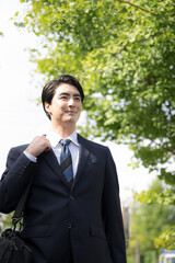  屋外の道路を歩きながら営業の外回りや取引先への訪問に向かうスーツ姿の日本人男性サラリーマン、法人営業や転職のイメージクローズアップで見上げる © kapinon