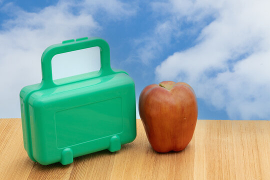 Lunch box with an apple outdoors on a table with sky