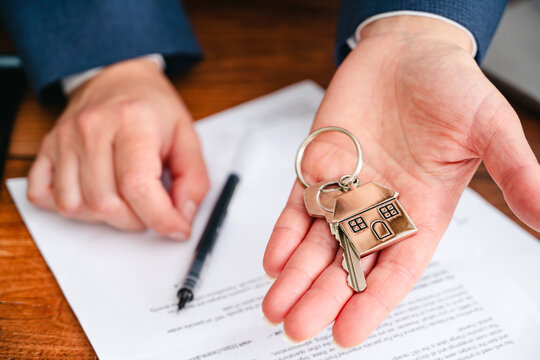 Real estate agent signing property contract with house keys on desk