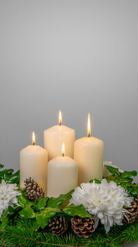 four white burning candles in a floral advent wreath isolated on gray studio background with copy space, social media format template for december holiday season
