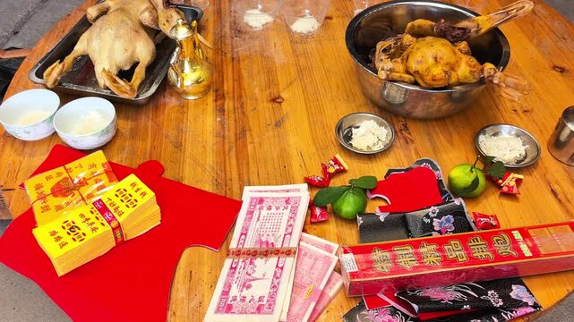 Heritage style: Traditional Chinese ancestor worship offerings on a wooden table during the Ghost Festival, featuring whole cooked chicken, duck, rice, and joss paper.
