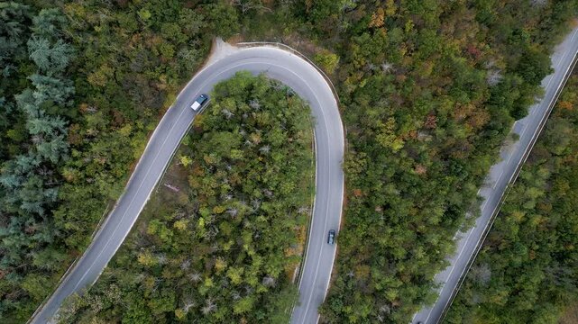 Aerial top view of winding hairpin road through autumn forest with moving car