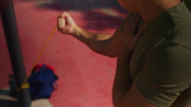 Man performs resistance band pulling exercises outdoors, building arm strength with focused functional training in bright sunlight.