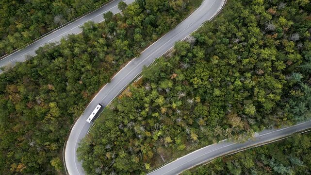Aerial top view of winding hairpin road through autumn forest with moving car
