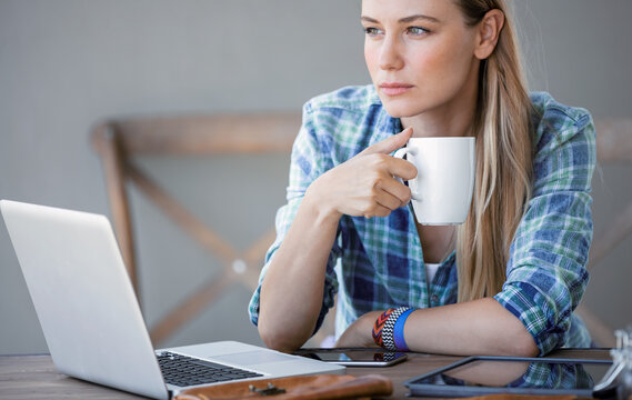 Thoughtful Young Woman Holding Coffee Cup Beside Laptop
