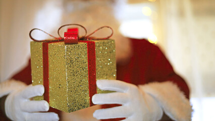 Santa presents a glittery gold box with a red ribbon and bow, bringing festive gift packaging to a Christmas retail theme centered on holiday shopping and the tradition of giving wrapped presents. © M.IVA