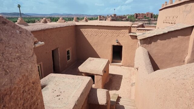 High-angle view looking down into an interior courtyard with traditional mud brick walls, doorways, and stair structures inside an ancient desert Kasbah fortress in Ouarzazate, Morocco