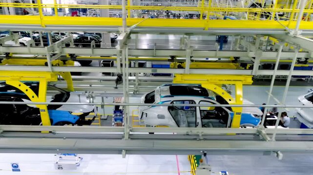 Automotive factory assembly line shows unfinished vehicle car chassis being built robotic arms, body hanging overhead yellow conveyor production line system structure advanced manufacturing equipment