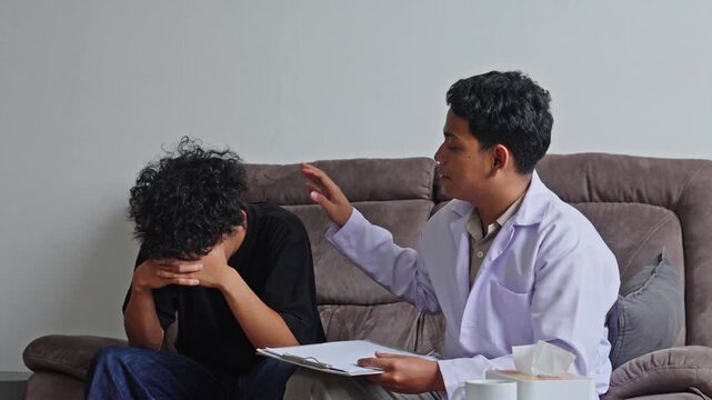Doctor comforting crying young man by touching his shoulder during PTSD therapy session