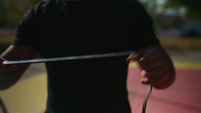 Man untangles and stretches a resistance band while preparing for focused outdoor fitness training on a sports court.