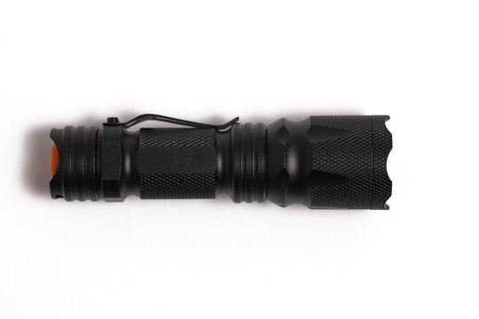 Top view black metal tactical flashlight lying horizontally on clean white background.