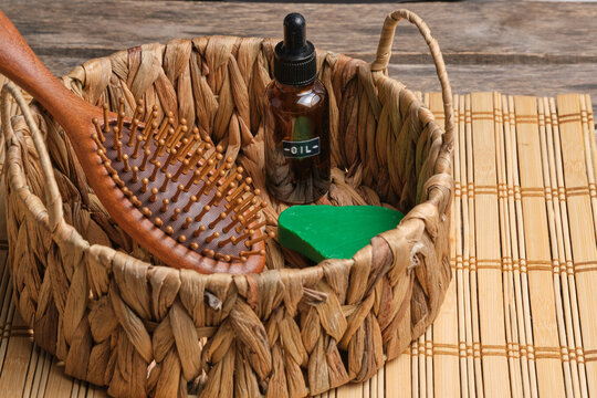 Eco grooming set with wooden hairbrush, glass oil dropper bottle, and soap in woven basket.
