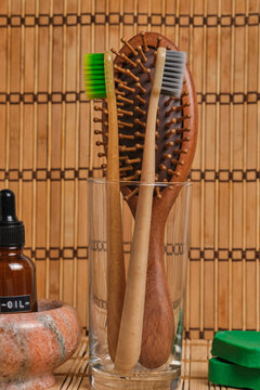 Close up eco wooden toothbrushes and hairbrush in glass with cosmetic oil on bamboo backdrop.