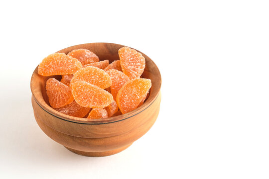 Side view round wooden bowl filled with sugary orange citrus jelly candies isolated on white.
