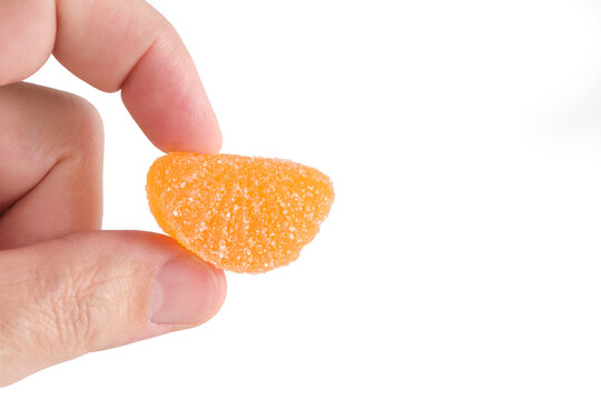 Fingers holding bright orange sugar coated citrus jelly candy isolated on plain white background.