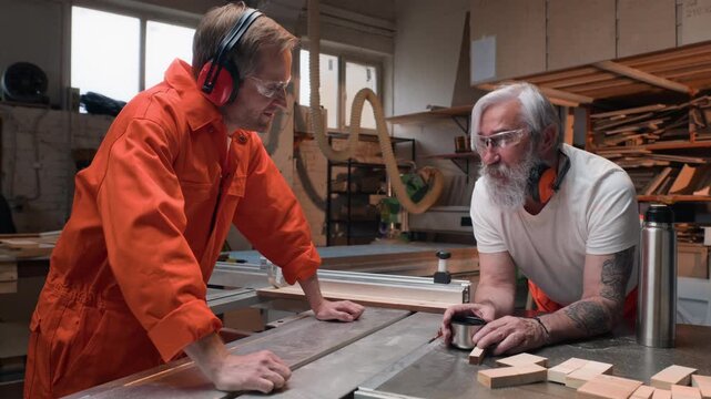 Senior Caucasian carpenter talking with young adult Caucasian apprentice during break in prison woodworking workshop. Footage ideal for vocational training and craftsmanship campaigns