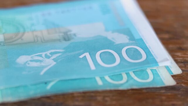 Horizontal video close up. Hand counts Serbian cash money on wood table. One hundred. Blue paper banknote 100 dinar bill. Concept of salary, budget, pay tax, bribe, trip, loan, wages, debt, credit