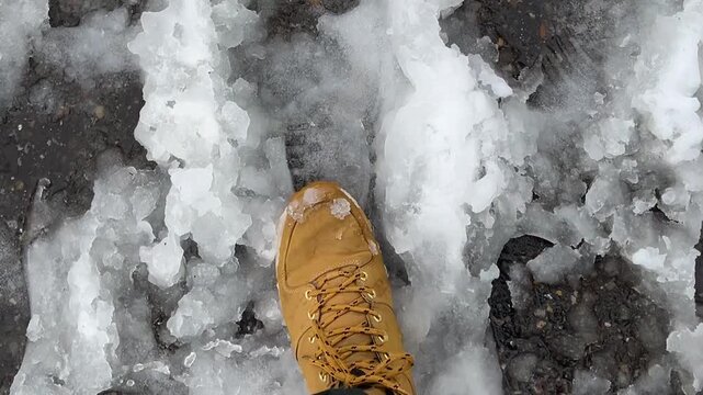 Street city video close up. Top view. Male legs. Man person wearing yellow brown boots walks on melting white snow and ice slush covering wet asphalt. Cold winter season. Travel, hiking. New Year 2027