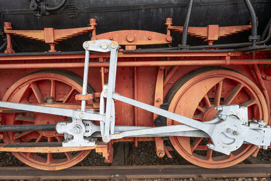 Close-up of red driving wheels and white connecting rods on a historic steam locomotive, showing weathered metal, rivets and traditional railway engineering