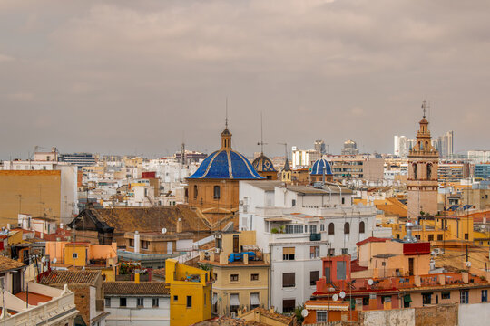 Scenic panoramic view on historic old town rooftops of Valencia, Spain, featuring iconic blue-tiled dome and  baroque bell tower of Santa Catalina church under warm evening sky.