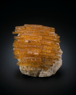 A cluster of orange wulfenite mineral crystals on a light colored matrix, showcasing sharp tabular crystal formations against a dark background