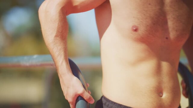 Muscular man performs tricep dips on outdoor parallel bars in slow motion during a calisthenics strength workout.