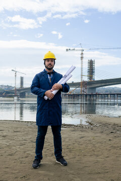 Construction engineer holding blueprints at a riverside bridge project