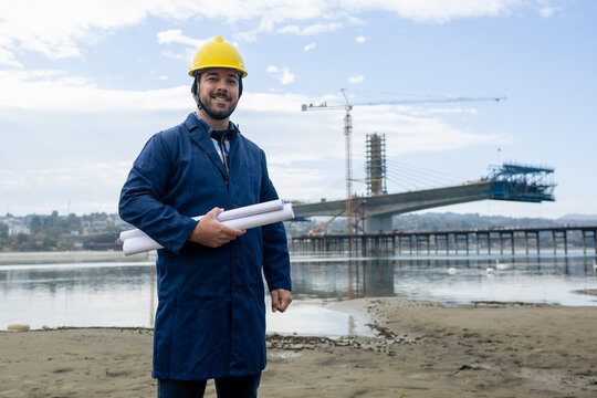 Construction engineer holding blueprints at a bridge project