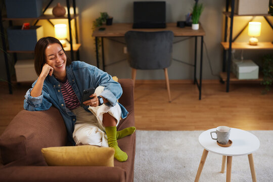 Smiling woman relaxing on a sofa and checking her smartphone