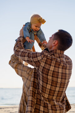 Father lifts his baby at the beach in a tender moment beneath the open evening sky