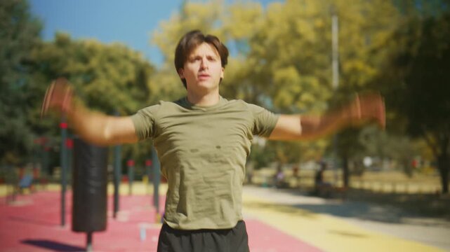 Man performs jumping jacks during an outdoor workout warm up, then catches his breath and shakes out his arms at a calisthenics park.