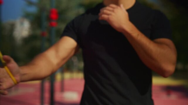Athletic man stretches a resistance band repeatedly during outdoor strength training at a calisthenics park.