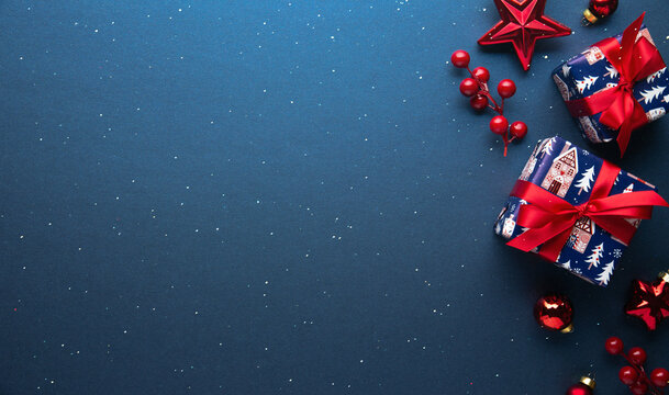 Blue Christmas and Happy New Year holiday background with gift boxes, red ribbon bows and festive red ornaments, flat lay with copy space. Greeting card.