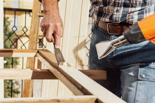 Carpenter using heat gun and wood scraper removes paint from old wooden window. Construction industry, carpentry. Restoration. 