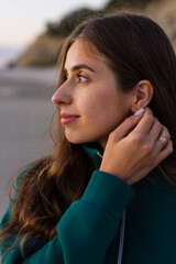 Woman adjusting a small earring in warm evening light during a quiet moment outdoors © Тарас Белецкий