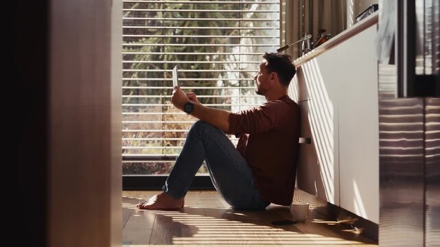 Side view of man using smart home app sitting on floor.