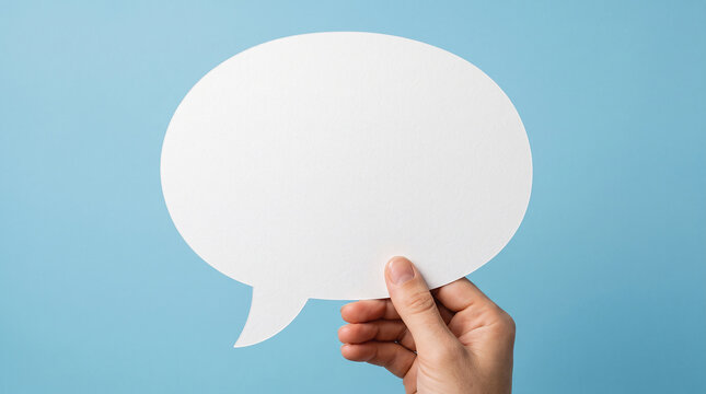 One hand holding oversized blank white speech bubble cutout, blue background, clean commercial mockup. Communication concept. Close-up.