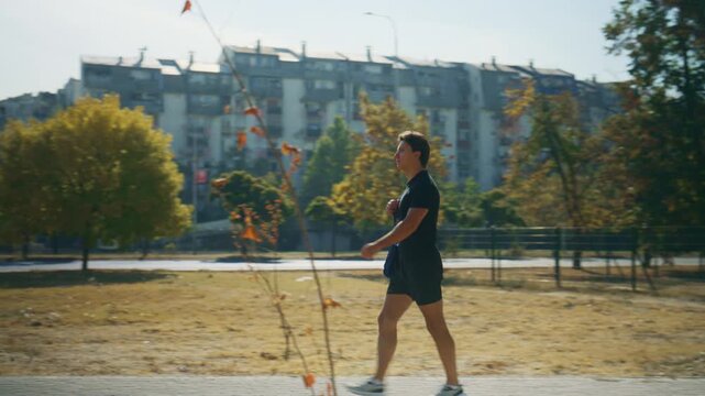 Man walks to the gym carrying a workout bag along a sunny park path, showing fitness training and an active daily routine.