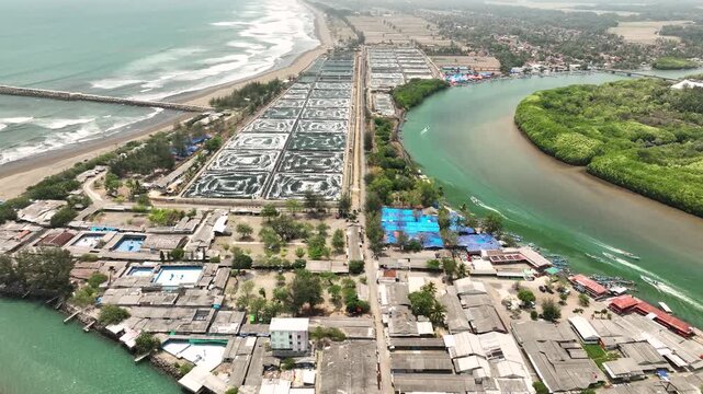 Aerial view of the Cilacap Shrimp Farm featuring aquaculture ponds, coastal village buildings, and a river flowing into the sea in Nusawungu, Central Java, Indonesia.