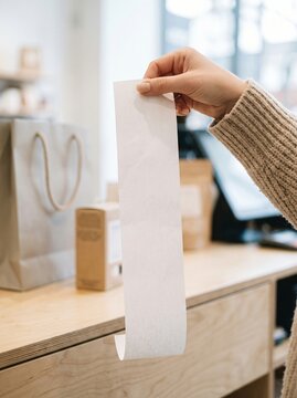 A person's hand holding a long white paper receipt in a retail store setting.