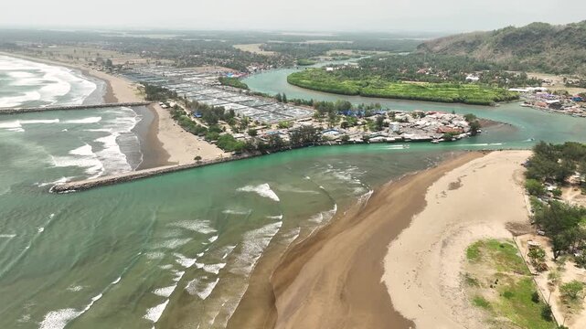 Aerial view of the Cilacap Shrimp Farm at the river mouth, featuring aquaculture ponds, sandy beaches, breakwaters, and lush coastal vegetation in Nusawungu, Central Java, Indonesia.