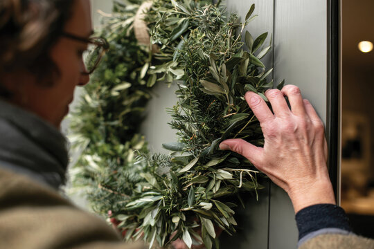 An individual carefully positioning a beautiful green wreath on a door, representing the welcoming spirit of home and the personal touch of seasonal decor.