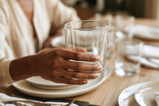 A stylishly dressed woman extends her hand, holding a clear glass of water, set against a beautifully arranged dining table. The ambiance is calm and inviting.