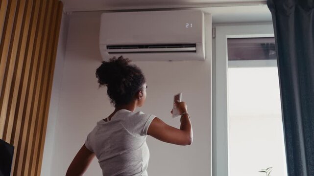 Young woman setting home temperature using air conditioner remote.