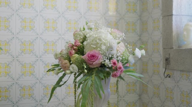Church flower arrangement in Portugal with gypsophila, lisianthus and hanging amaranthus in a white vase, a granite window ledge and small bust beside it.