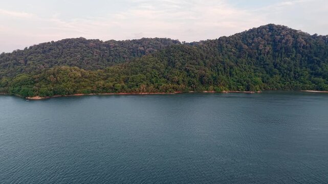 Move over sea toward Lush Green Forested Hillscape Under Overcast Sky